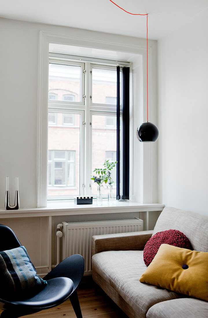 Helle Couch und schwarzer Designerstuhl vor Fenster im Wohnzimmer