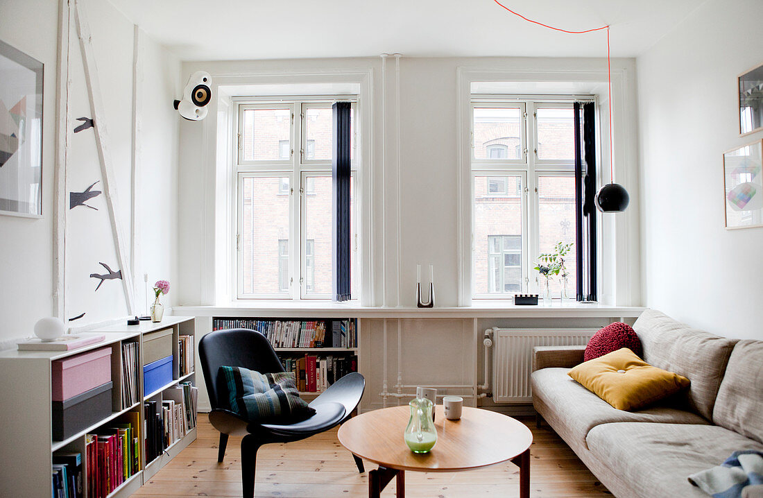 Sandfarbene Couch, Coffeetable und Designerstuhl im Wohnzimmer, Regale mit Büchern
