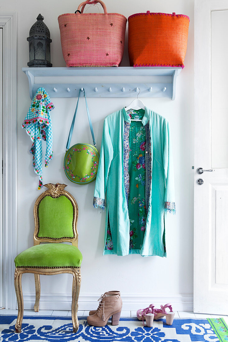 Colourful baskets, a lantern and clothing on a coat rack on the wall with a green chair below it