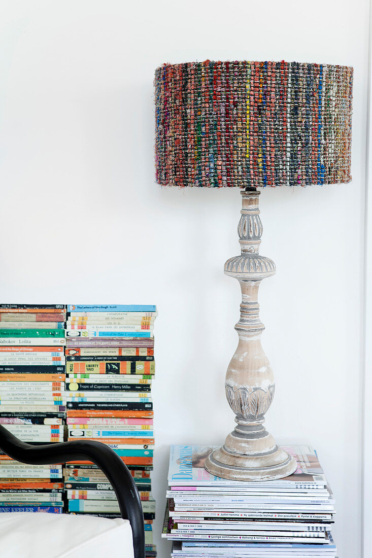 Table lamp with carved wooden base and colored lampshade on a pile of magazines