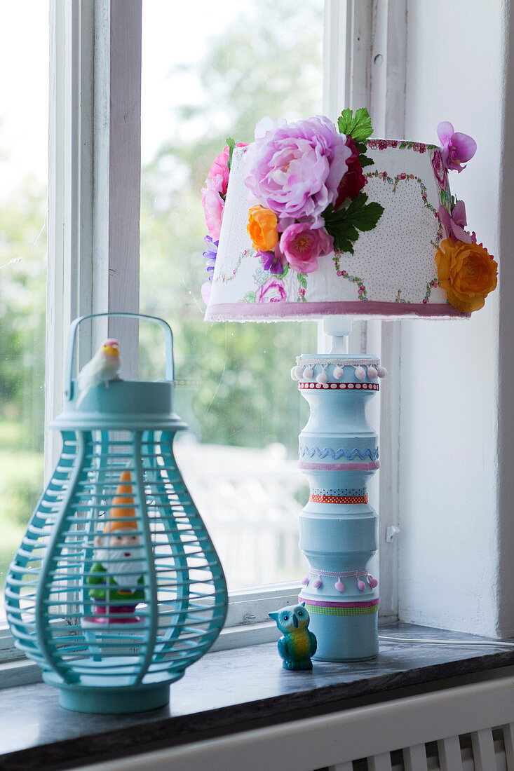 Turquoise lantern with garden gnome and table lamp with a decorated lampshade on a window sill