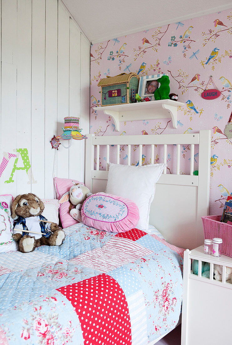 White wooden bed with patchwork blanket and plush stuffed animals in a girl's room