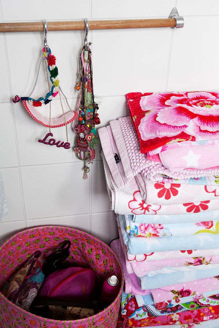 A stack of colourful towels, jewellery and a basket of cosmetic utensils