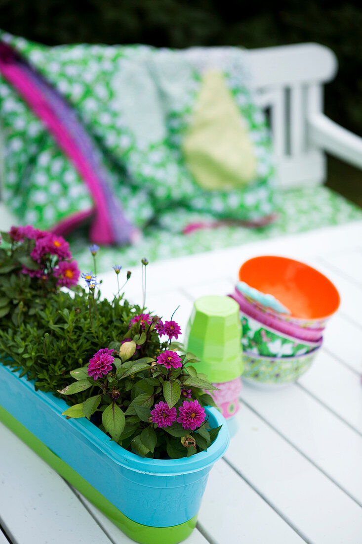 Blumenkasten, Becher und bunte Schalen auf Gartentisch