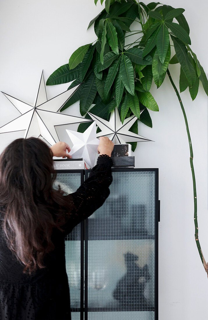 Woman placing paper stars on top of cabinet next to houseplant
