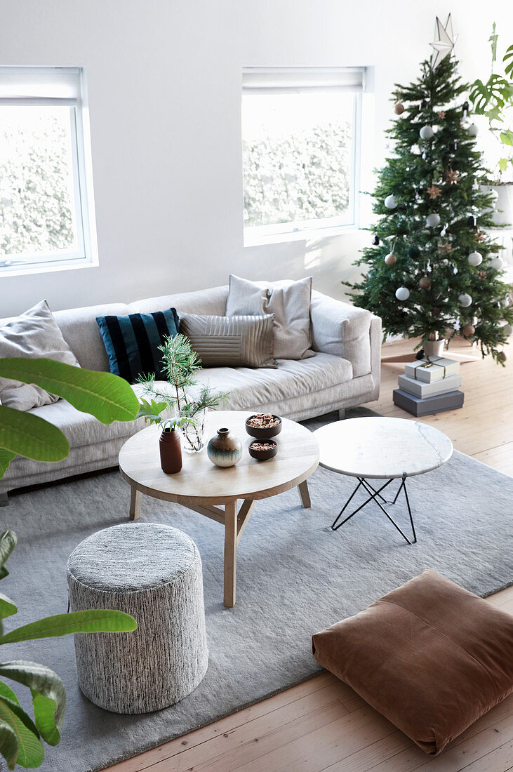 Pale sofa and round tables on grey rug next to decorated Christmas tree