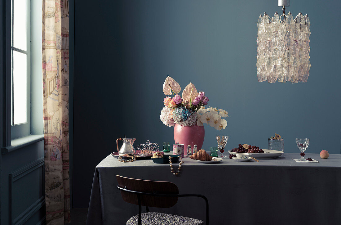 Feminin gestalteter Frühstückstisch mit Blumenstrauß und Schmuck, darüber Designer-Kronleuchter