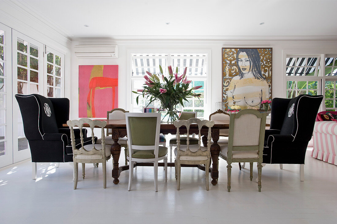 Various chairs and wingback armchairs around dining table and modern artworks on white wall