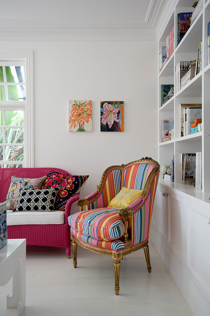 Antiker Sessel mit gestreiftem Bezug und pink lackiertes Rattansofa vor Bücherregal