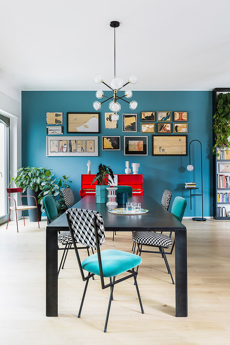 Dining table and upholstered chairs in front of gallery of pictures on blue wall