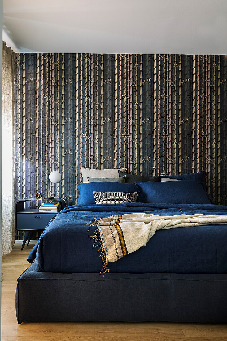 Dark blue bed in front of blue-patterned wallpaper in bedroom