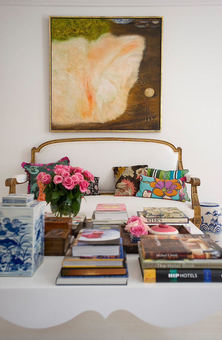 Blick über Couchtisch mit Büchern auf antikes Sofa mit weißem Bezug und Gemälde