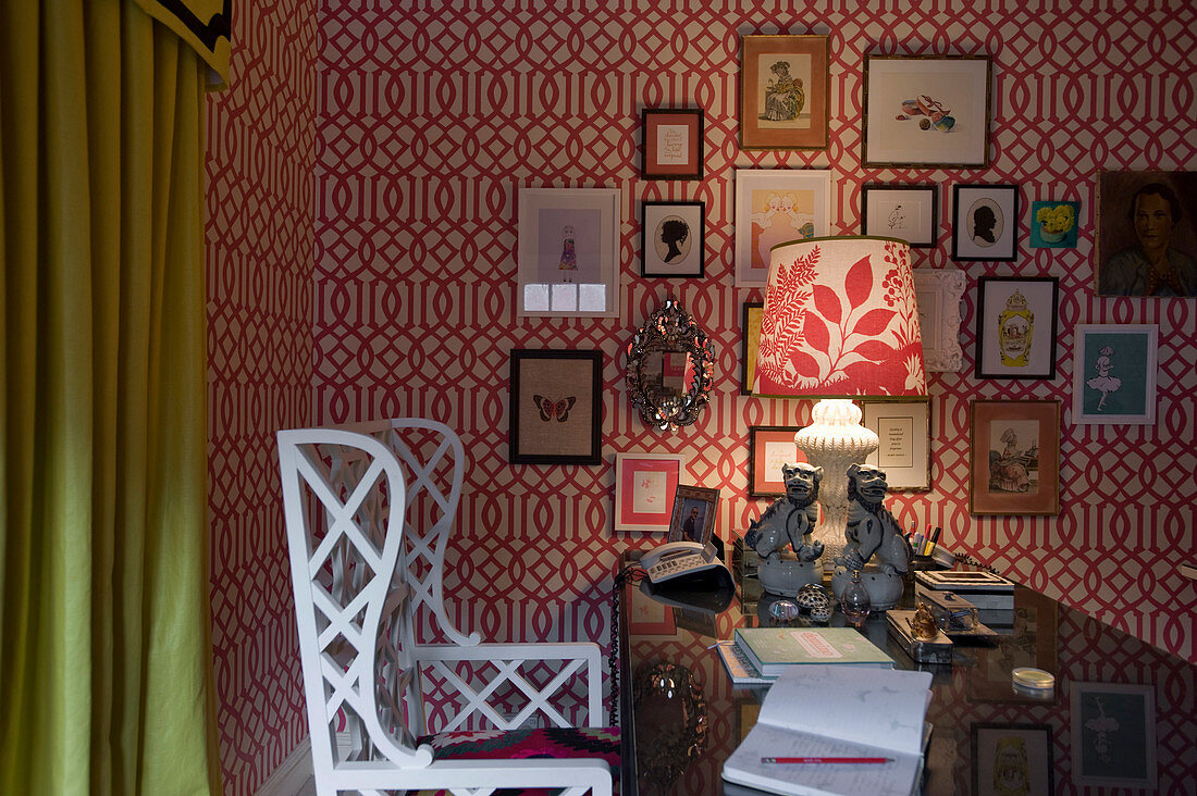 White wooden chair at desk in study with gallery of pictures on red-and-white wallpaper