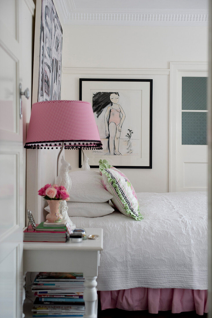 Bed with white bedspread, table lamp with gingham lampshade on bedside table and pictures on walls