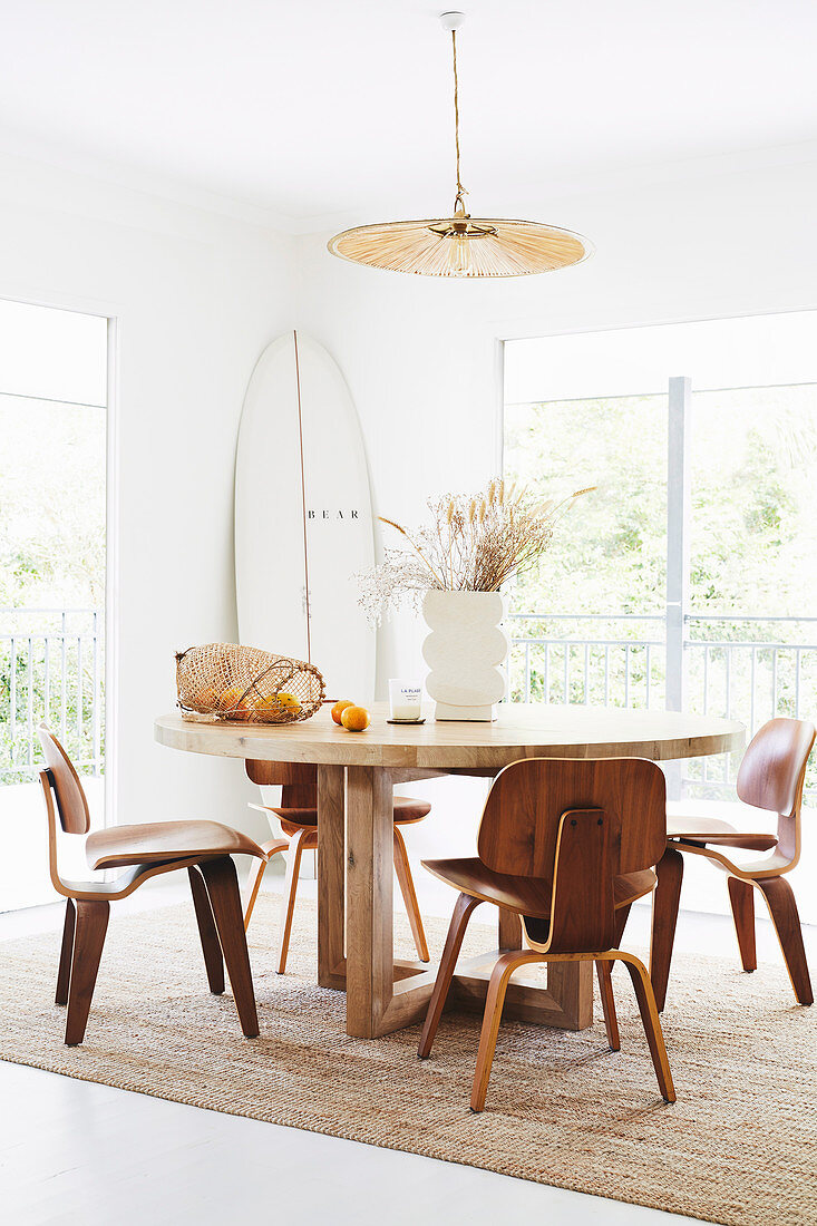 Round wooden table with classic chairs in a bright dining area, surfboard in the background