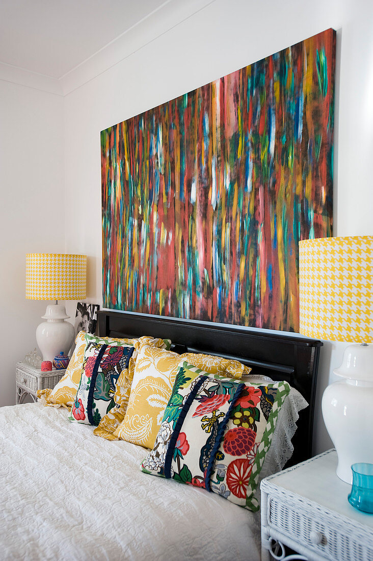 Colourful painting above bed with floral scatter cushions