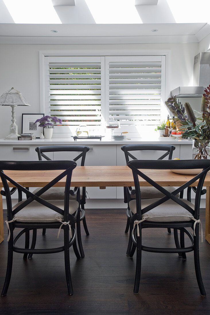 Black bistro chairs at wooden table in bright kitchen-dining room