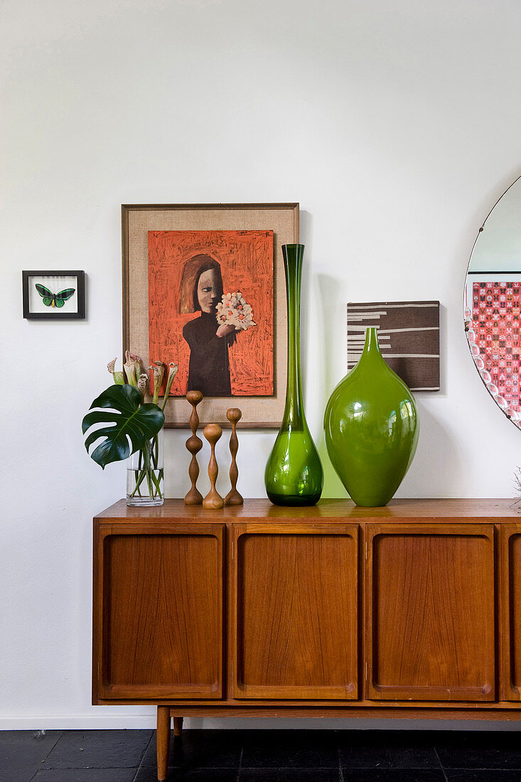 Retro Sideboard mit grünen Glasvasen, Kerzenhaltern und Pflanze, Kunstwerke an der Wand