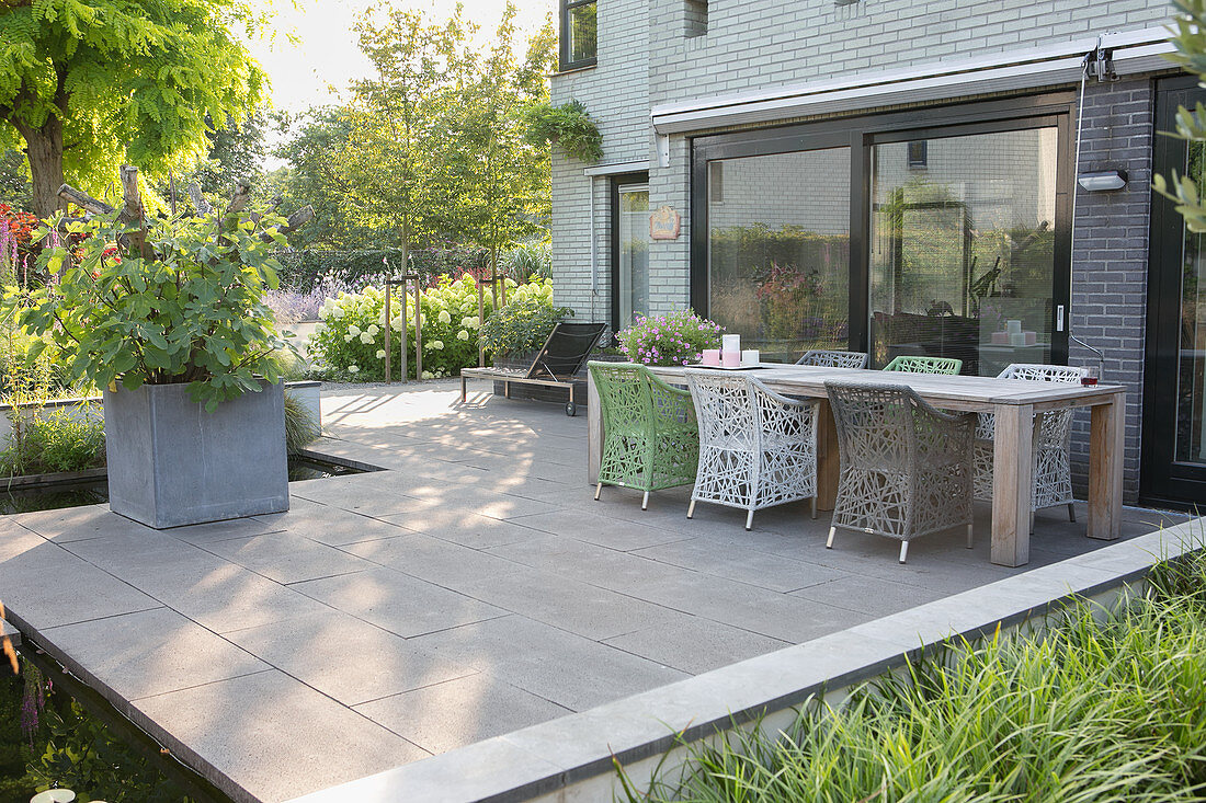 Holztisch und Designerstühle auf Terrasse mit Betonfliesen