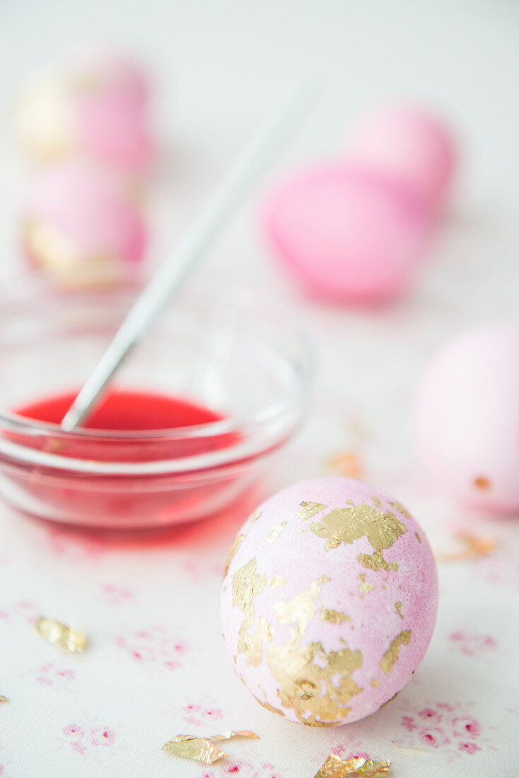 Rosafarbene Eier mit Blattgold und Schälchen mit Farbe