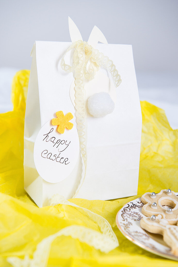 Osterhase mit Spitzenborte an einer Geschenktüte auf gelbem Papier