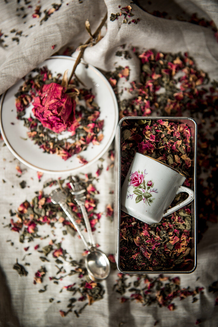 Cups with floral motif and dried rose petals in tin