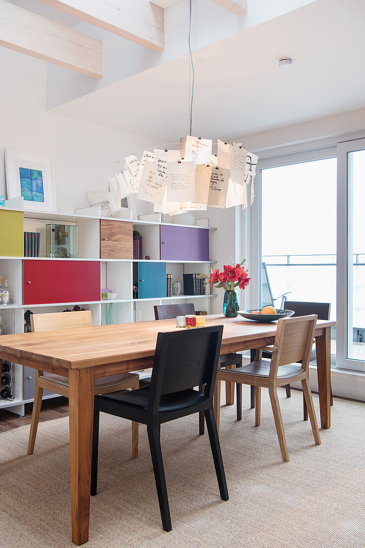 Designerleuchte überm Esstisch vor Regalwand mit farbigen Türen