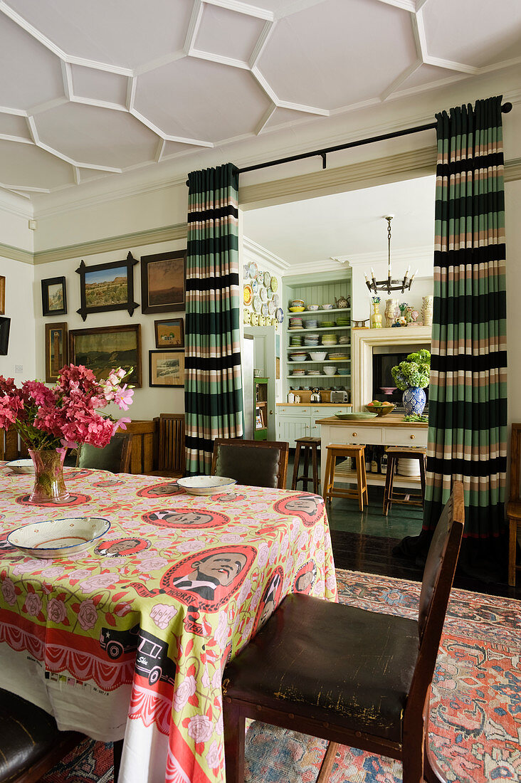 Südafrikanische Tischdecke mit Obama-Motiv auf Esstisch mit Vintage Lederstühlen, Blick durch offenen Vorhängen in die Küche