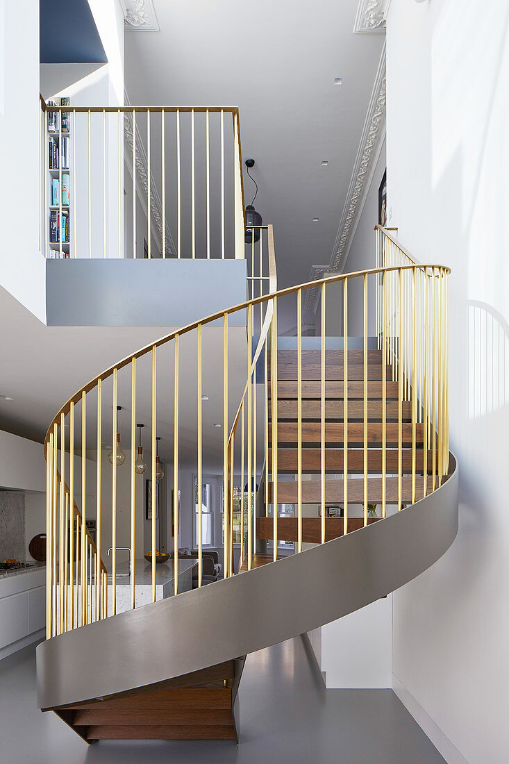 Spiral staircase with gold balustrades in open-plan interior
