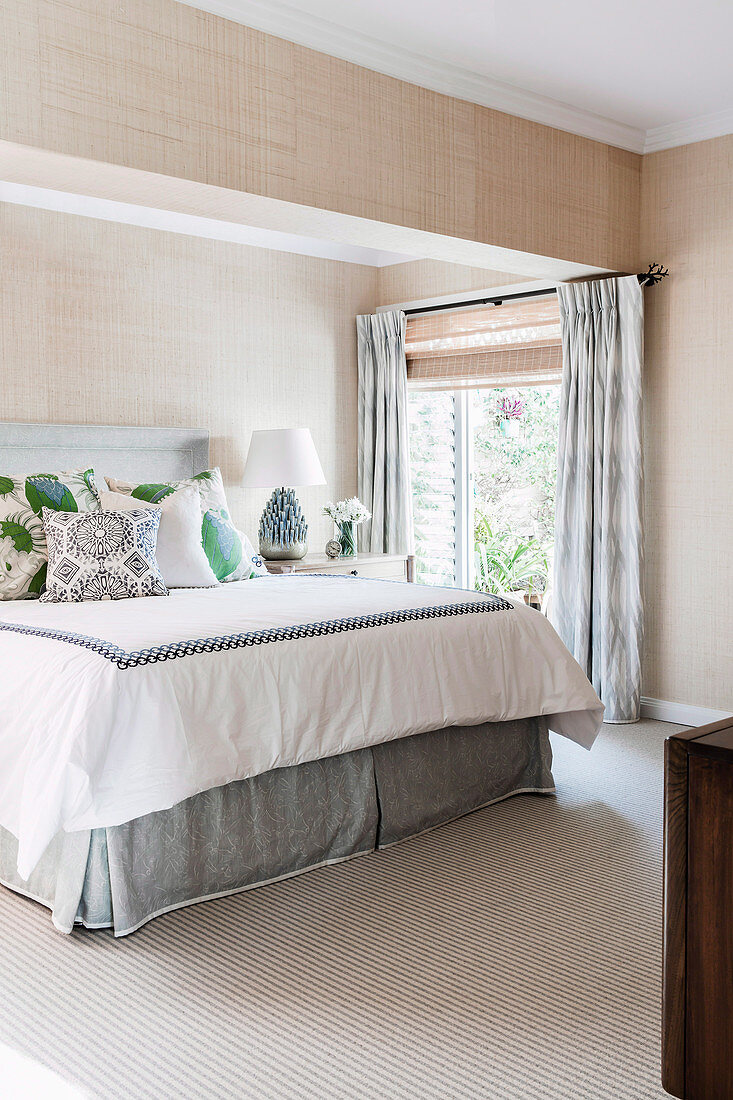 Double bed in bright bedroom with beige wallpaper