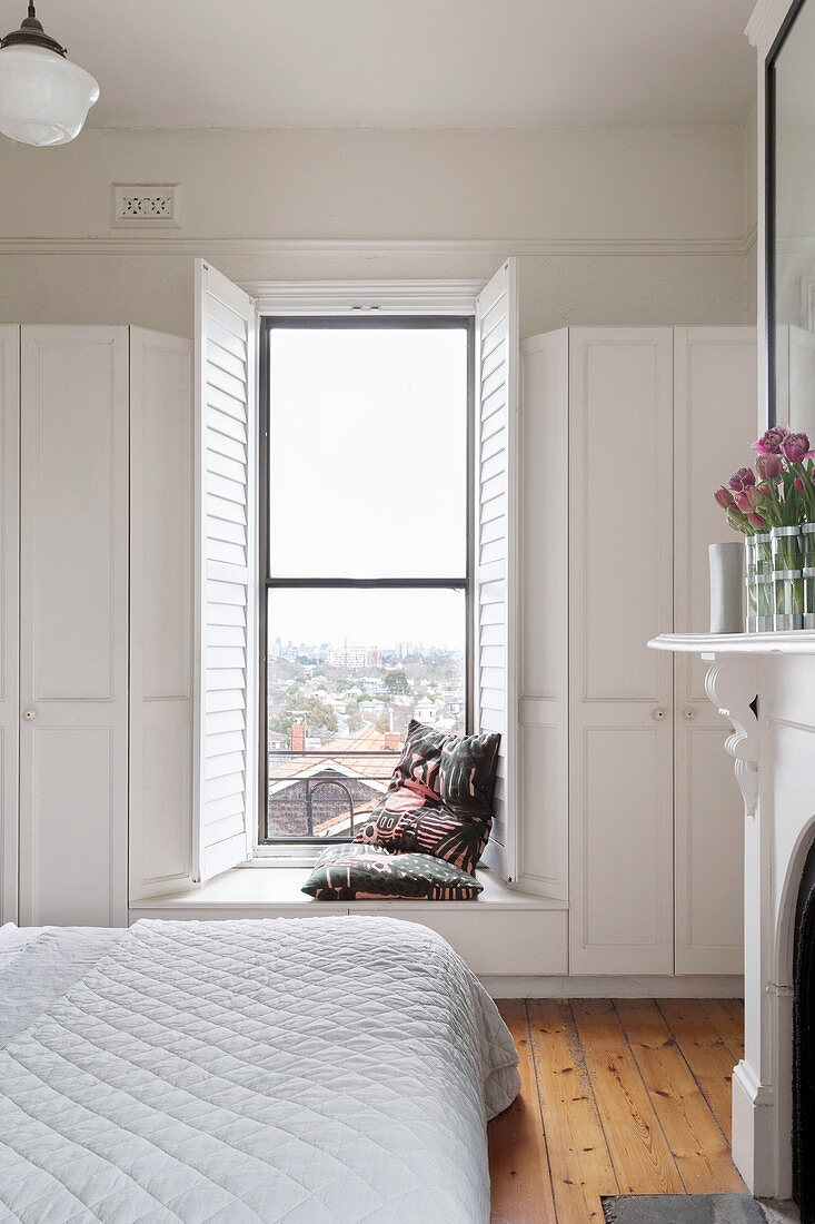 Doppelbett vor Fensterbank als Sitzbank in weißem Schlafzimmer