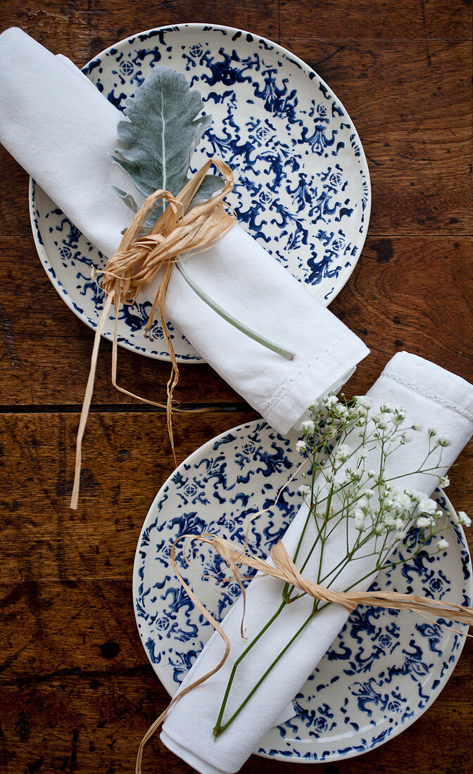 Two place settings with blue and white plates, and white napkins tied with straw and florals