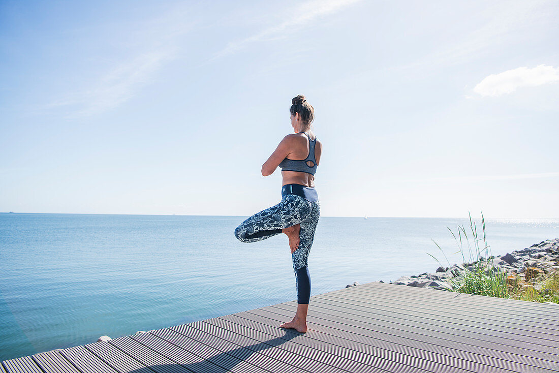Frau macht Yoga-Übung (Der Baum) am Meer