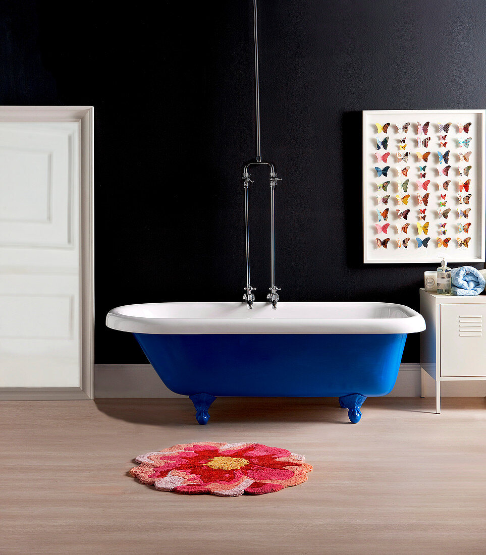 Blaue, frei stehende Badewanne vor schwarzer Wand, Papierschmetterlinge als Wanddekoration