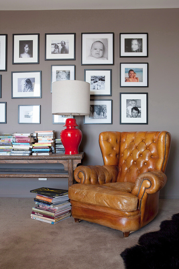 Vintage Ledersessel und Konsolentisch mit Tischleuchte und Bücher vor grauer Wand mit Fotogalerie