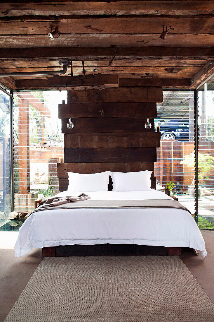 Bed against wall made of wooden planks in the bedroom with louvre windows