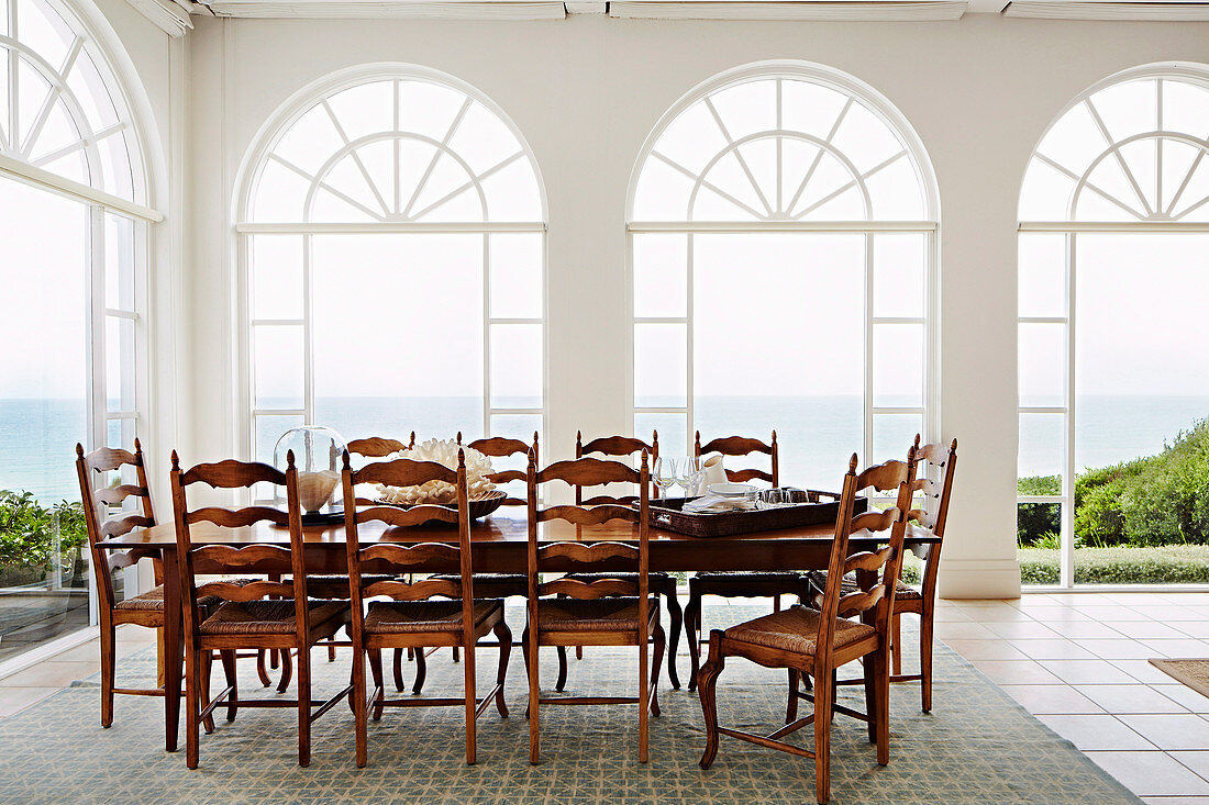 Long table with wooden chairs in front of arched window fronts with sea view