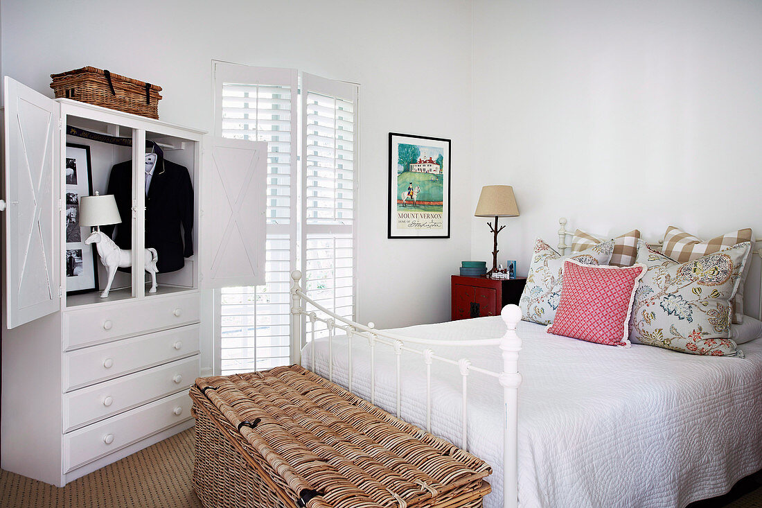 White bedroom with metal bed, wicker chest and open closet
