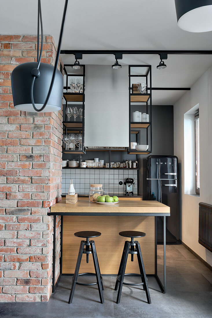Blick in offene Küche mit offenen Hängeregalen und Frühstückstheke neben Backsteinwand