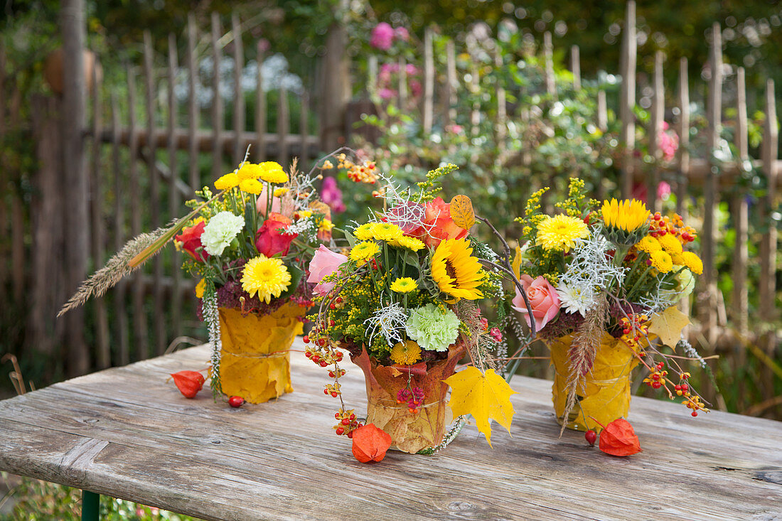 Blumensträuße mit Sonnenblumen und Chrysanthemen in mit Herbstlaub umhüllten Vasen