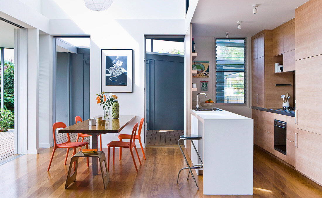 Dining table with orange chairs in front of open kitchen with counter