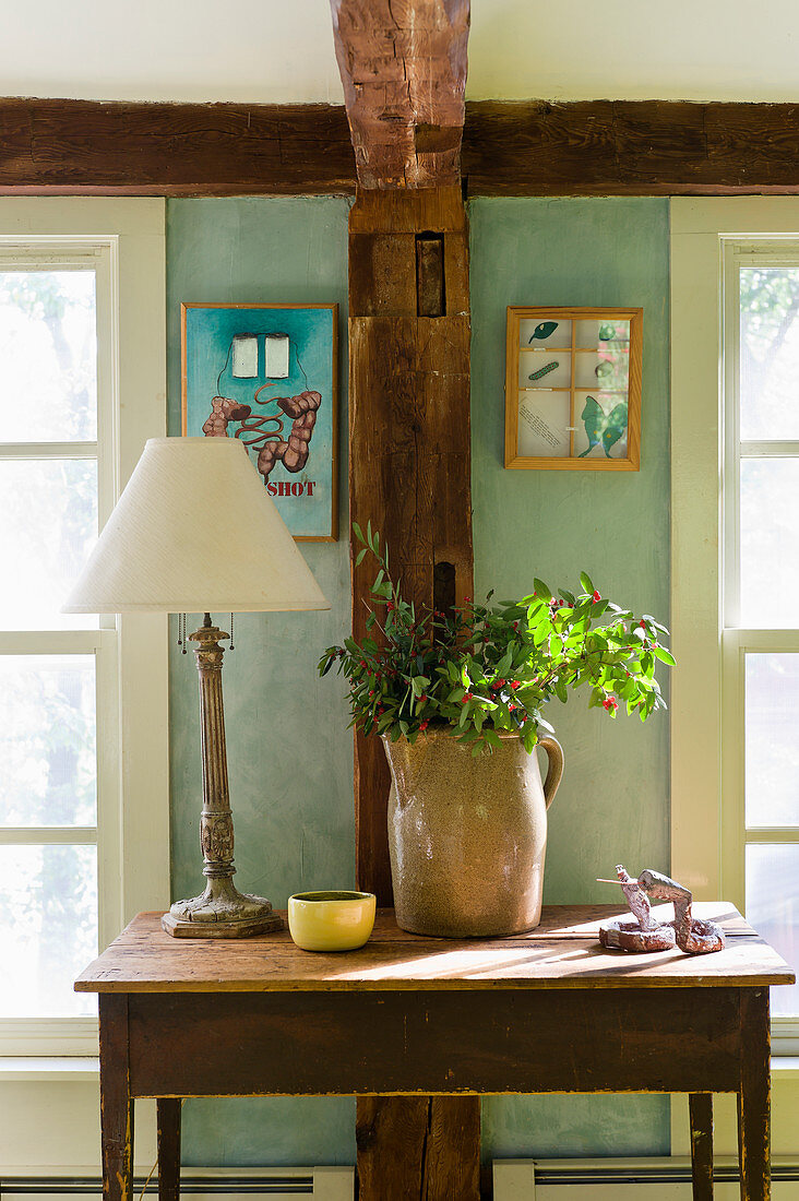 Branches in jug and lamp on old wooden table in front of wooden beam