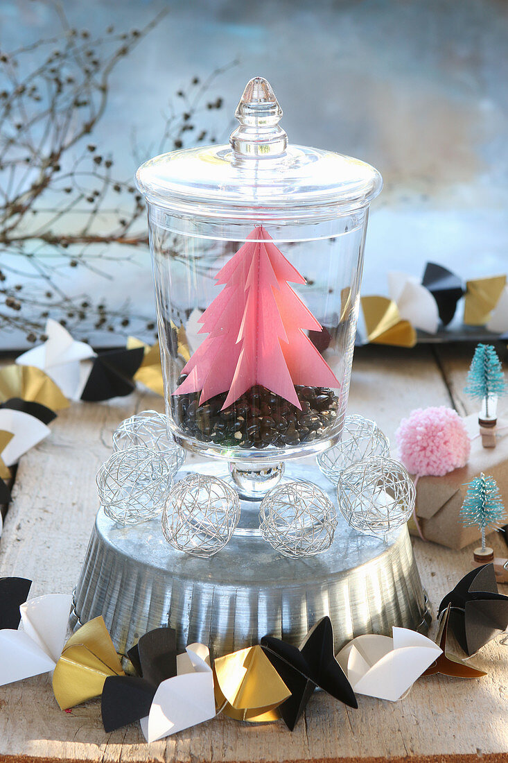 Pink paper Christmas tree in jar on top of cake tin with origami garland