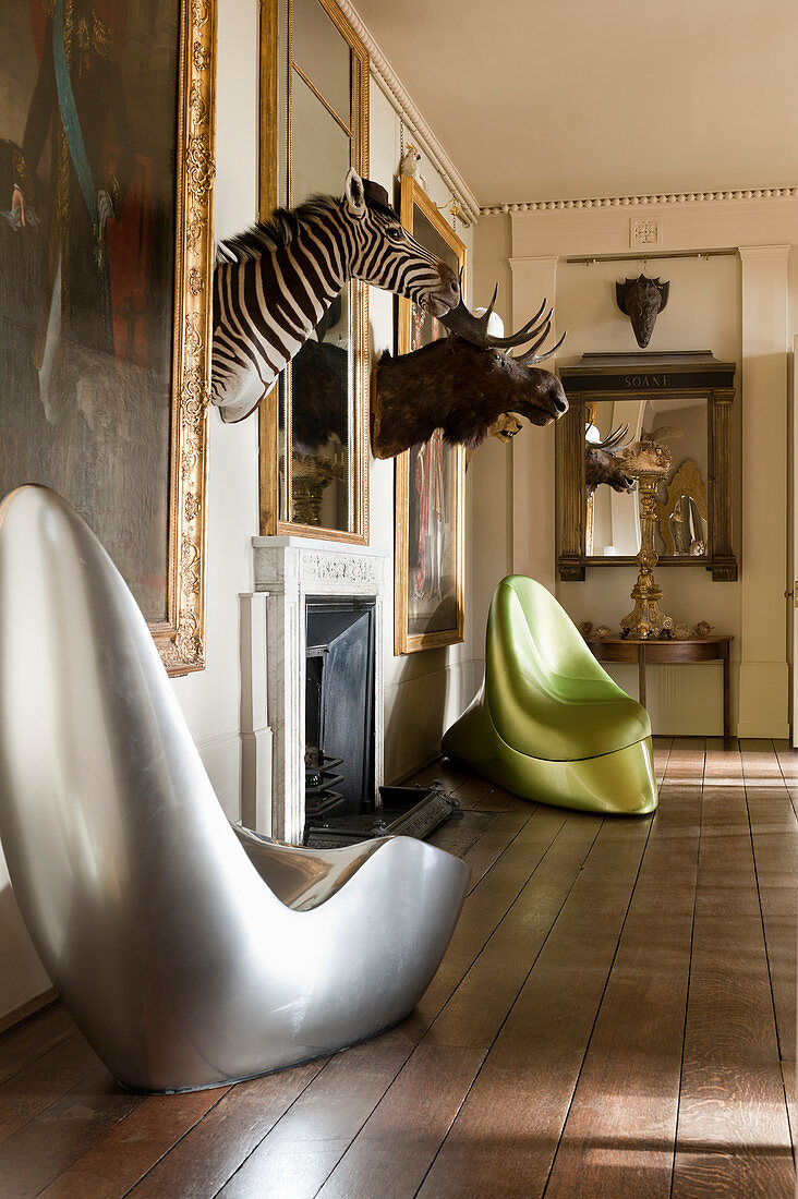 Silberner Stuhl und grüner, satinierter Acrylstuhl im Raum mit Elch- und Zebraköpfen