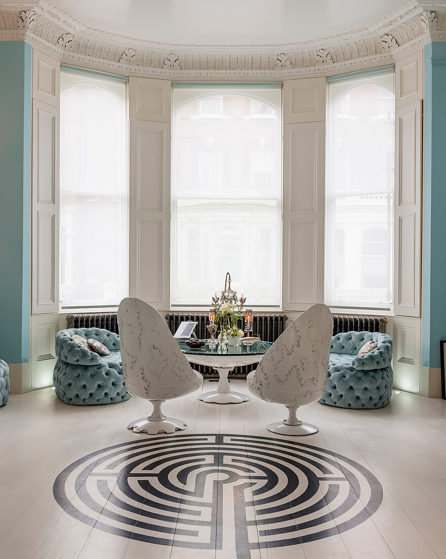 Erkerraum in Weiß und Himmelblau mit Sitzmöbeln, rundem Tisch und Labyrinthmuster auf Boden