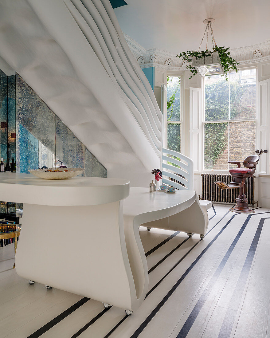 Weißer gebogener Designertisch und skulpturalem Treppengeländer in extravaganter Wohnung