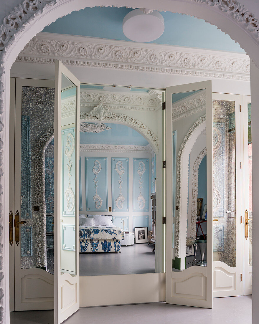 Tall wardrobe with mirrored doors in sky-blue bedroom with ornate stucco elements