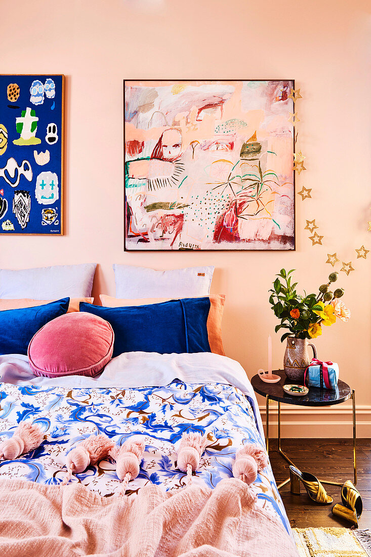 Schlafzimmer in Rosa- und Blautönen mit Quasten-Plaid, abstrakten Wandbildern und Weihnachtsdeko