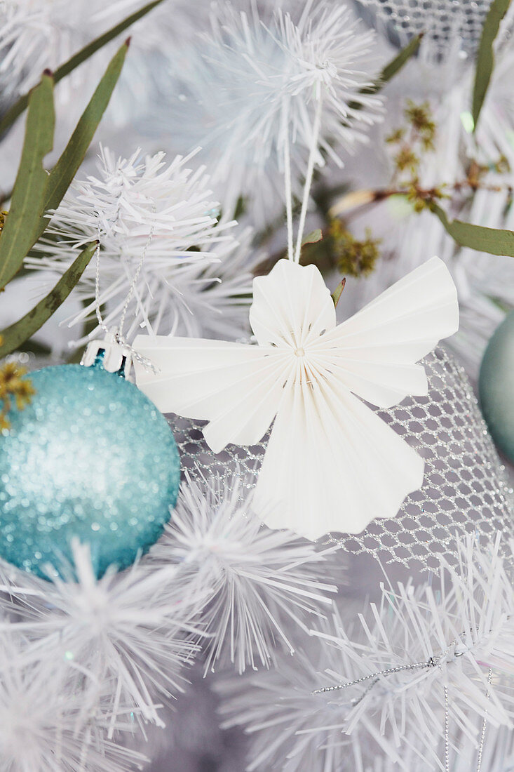 Paper angel next to ice blue Christmas ball in the fir tree