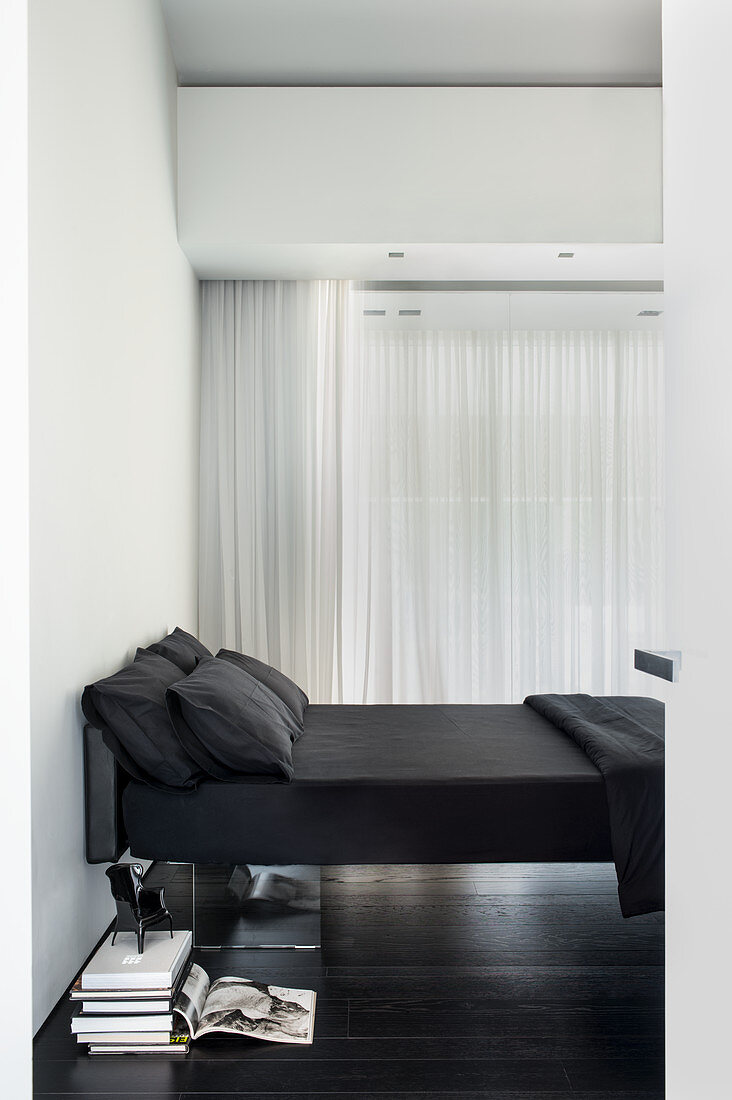 Blick auf Bett mit schwarzer Bettwäsche in weißem Schlafzimmer